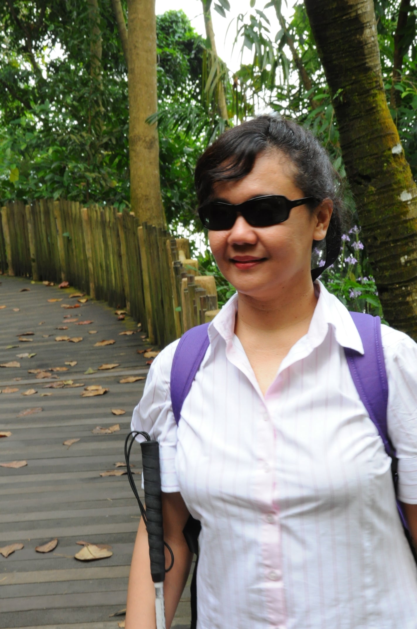 Sherri Eri, the blind writer, stands holding a white cane, smiling.