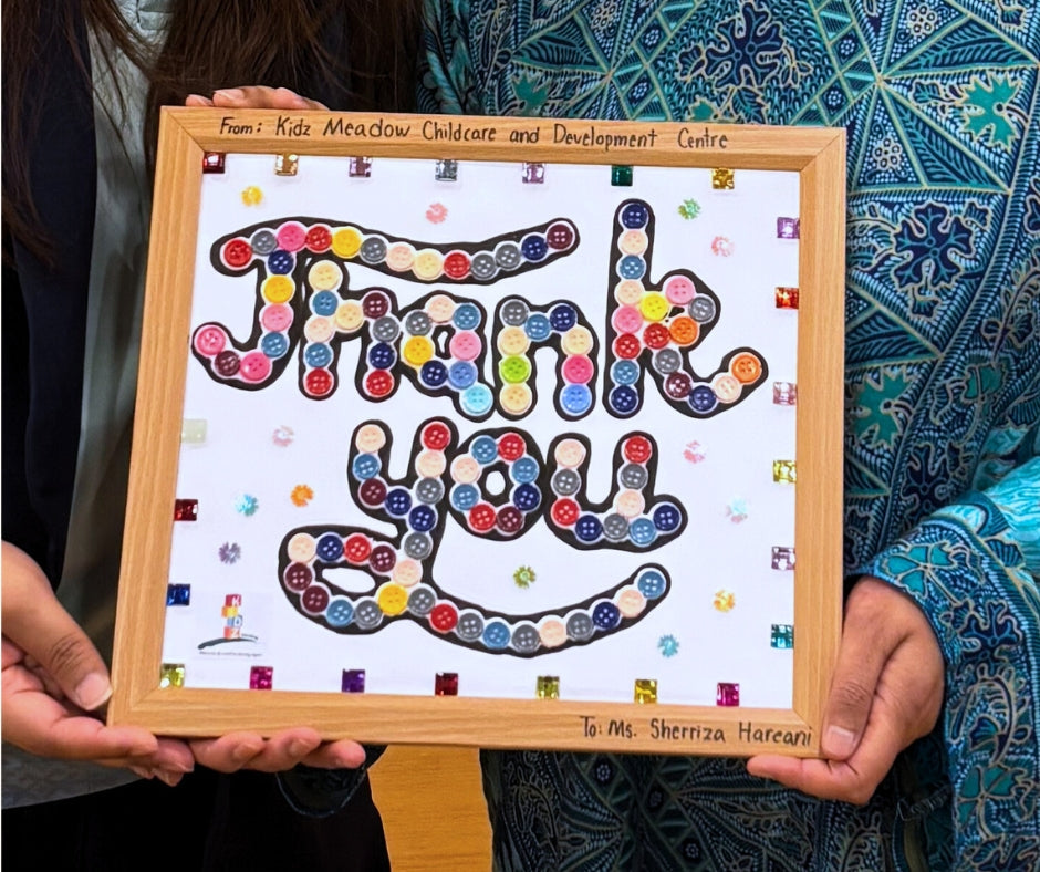 Author Sherri Eri holding a handcrafted sensory 'Thank You' gift from Kidz Meadow students. The button-covered frame allows the visually impaired author to 'see' their appreciation through touch.