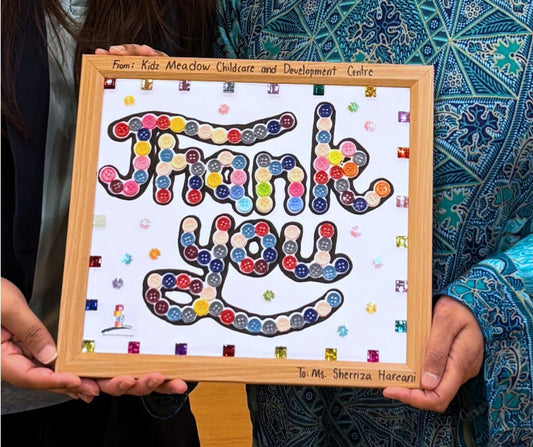Author Sherri Eri holding a handcrafted sensory 'Thank You' gift from Kidz Meadow students. The button-covered frame allows the visually impaired author to 'see' their appreciation through touch.